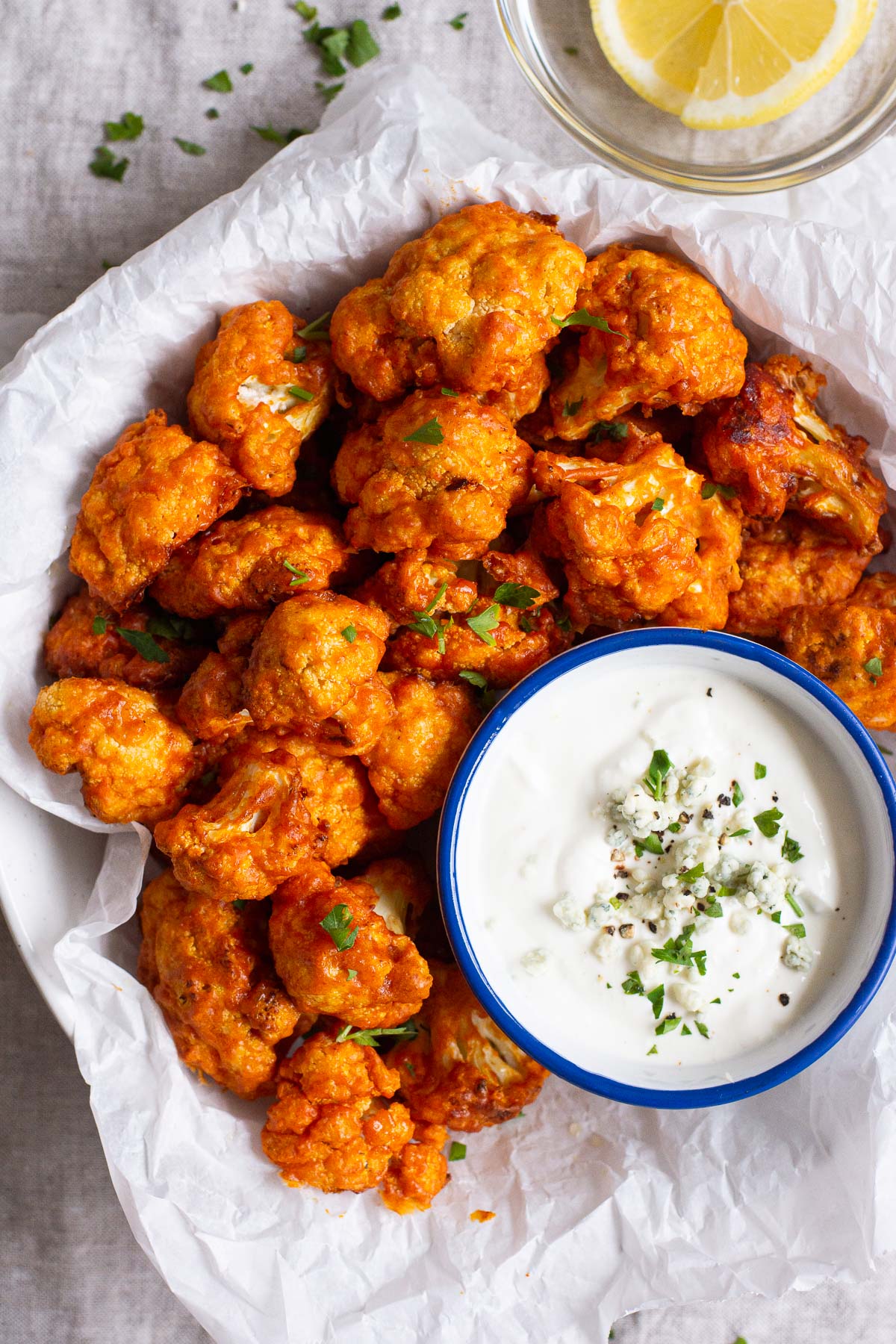 Air fryer buffalo cauliflower on parchment paper lined dish with blue cheese dip.