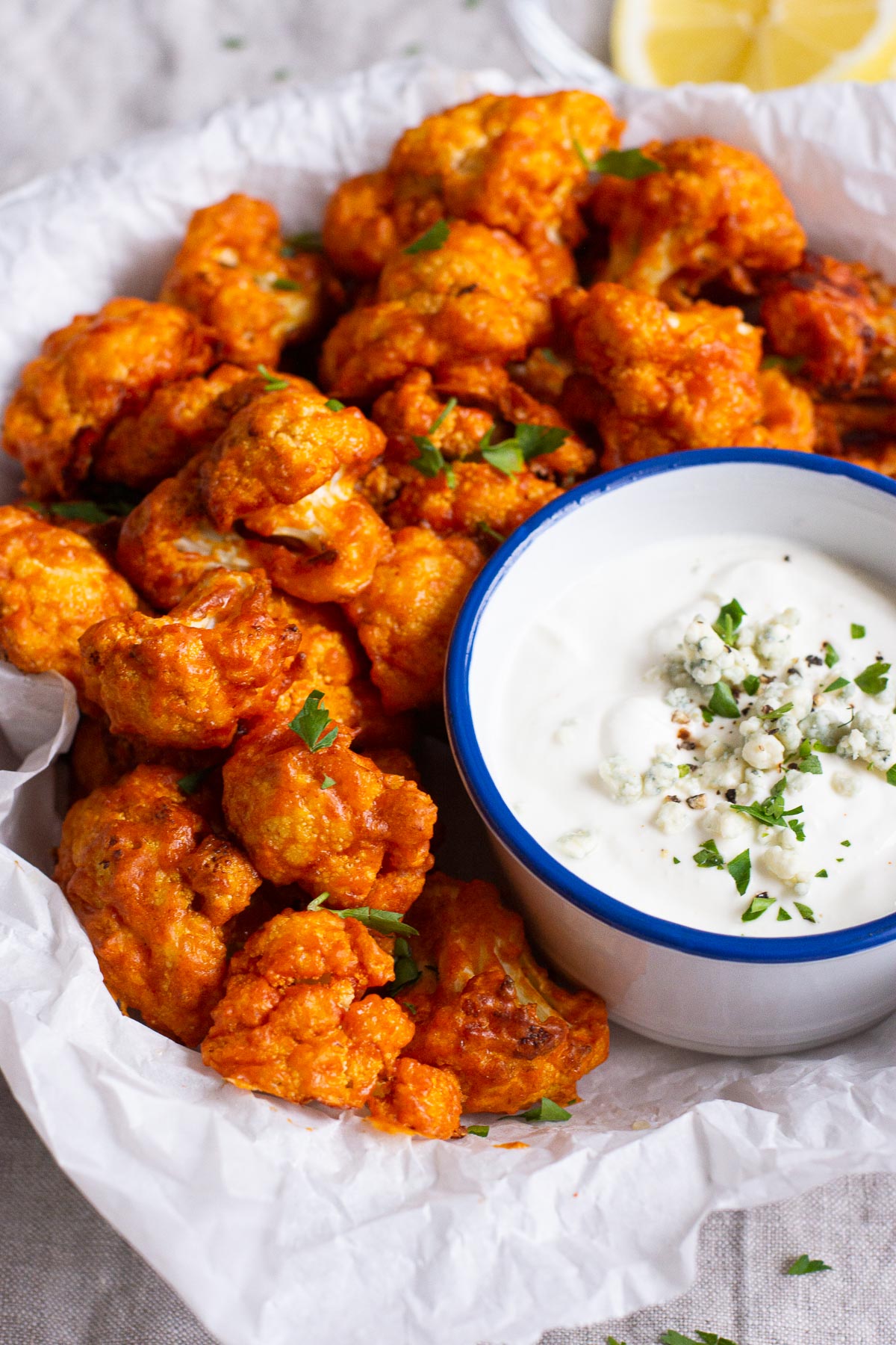 Air fryer buffalo cauliflower on a parchment lined dish with blue cheese dip. 