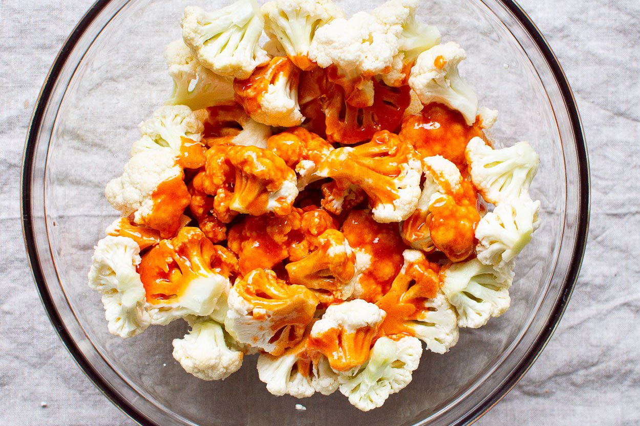 Cauliflower in a bowl with hot sauce drizzled over it.