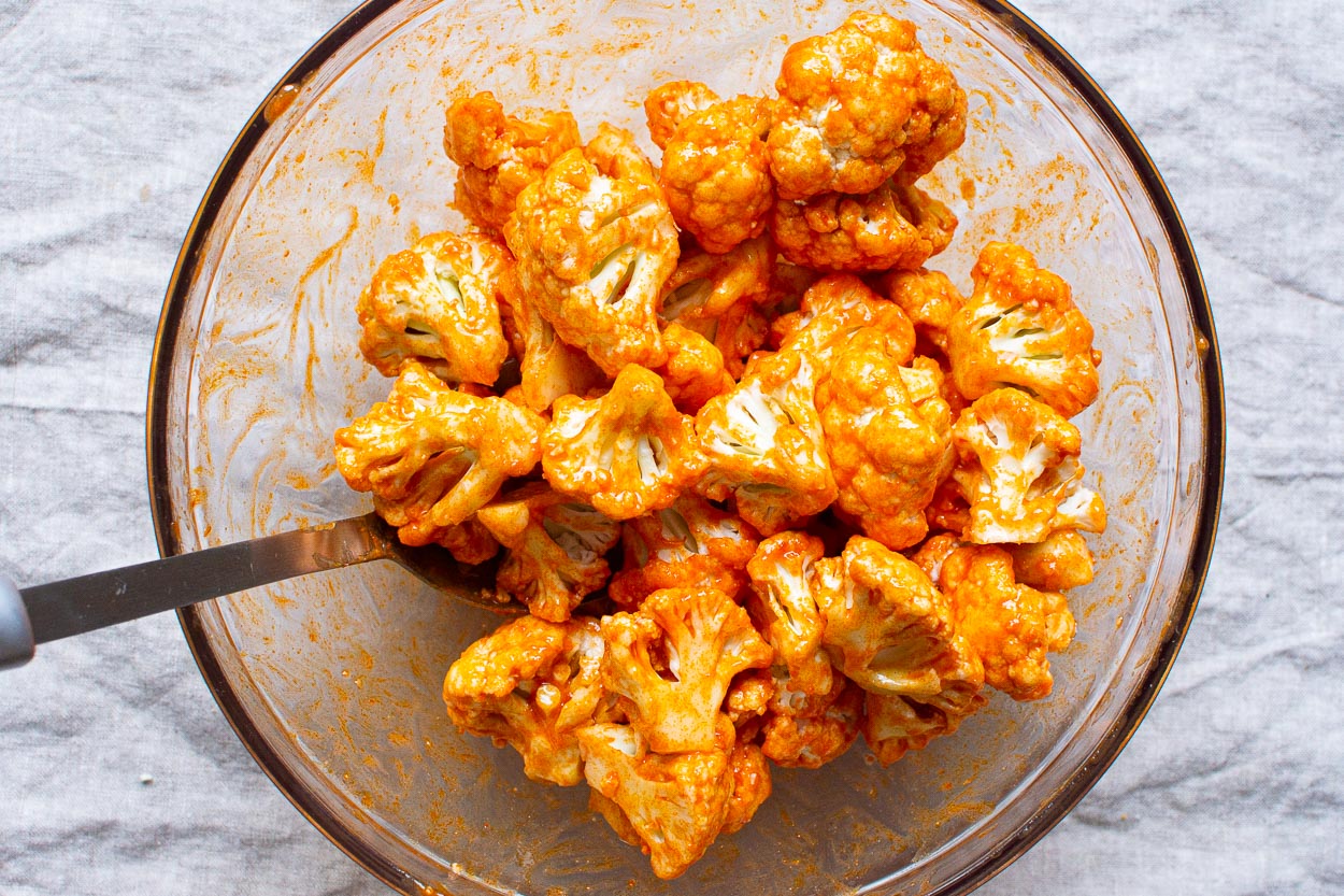 Spoon coating cauliflower florets with buffalo sauce in a bowl.