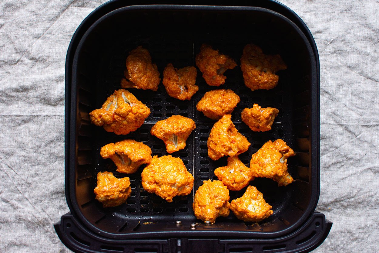 Uncooked and prepped cauliflower in air fryer basket.