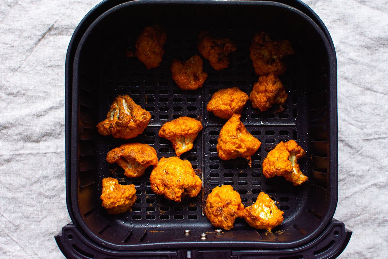 Air fried buffalo cauliflower in basket of air fryer.