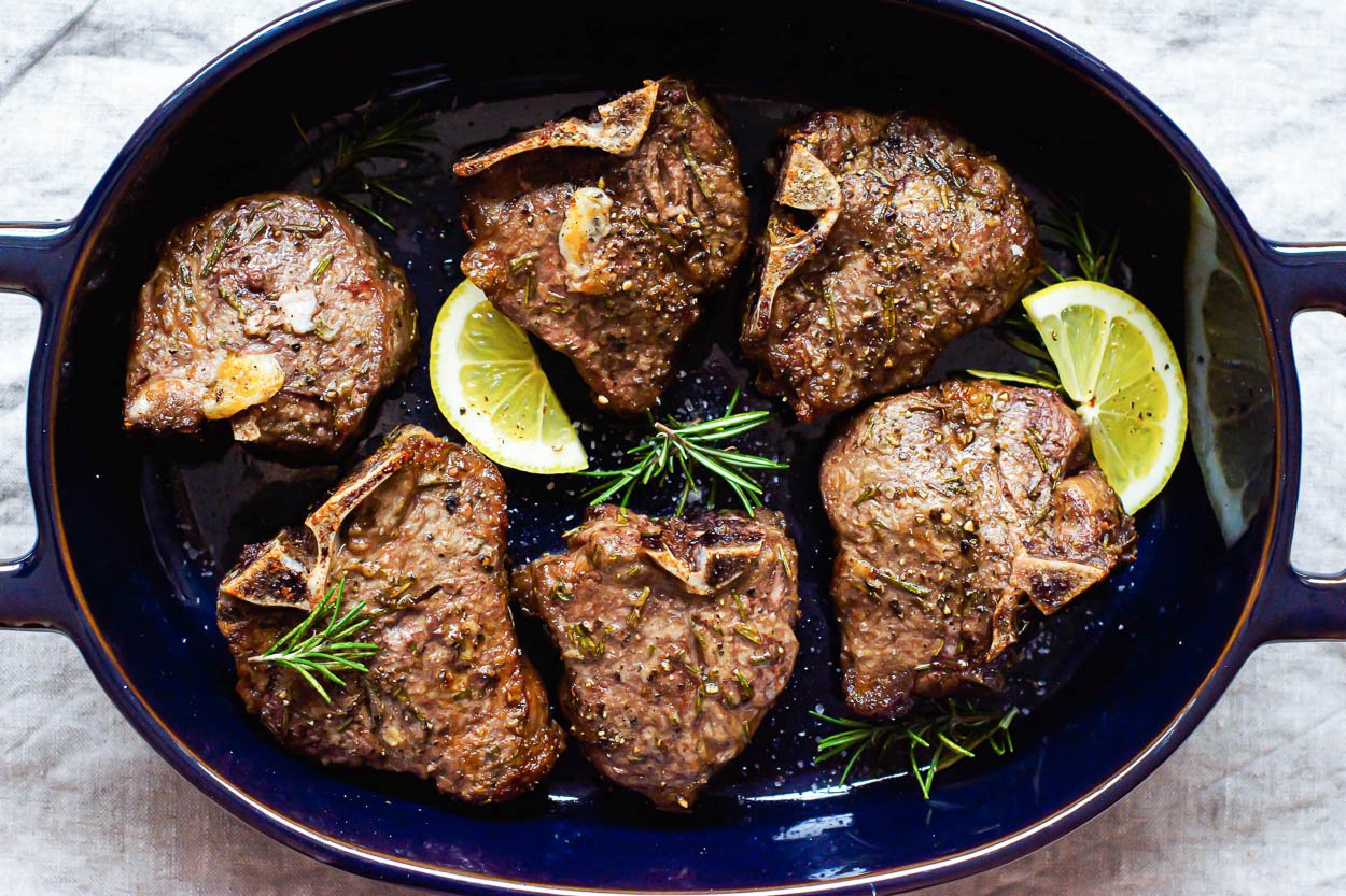 Air fryer lamb chops, rosemary, and lemon slices in serving dish.
