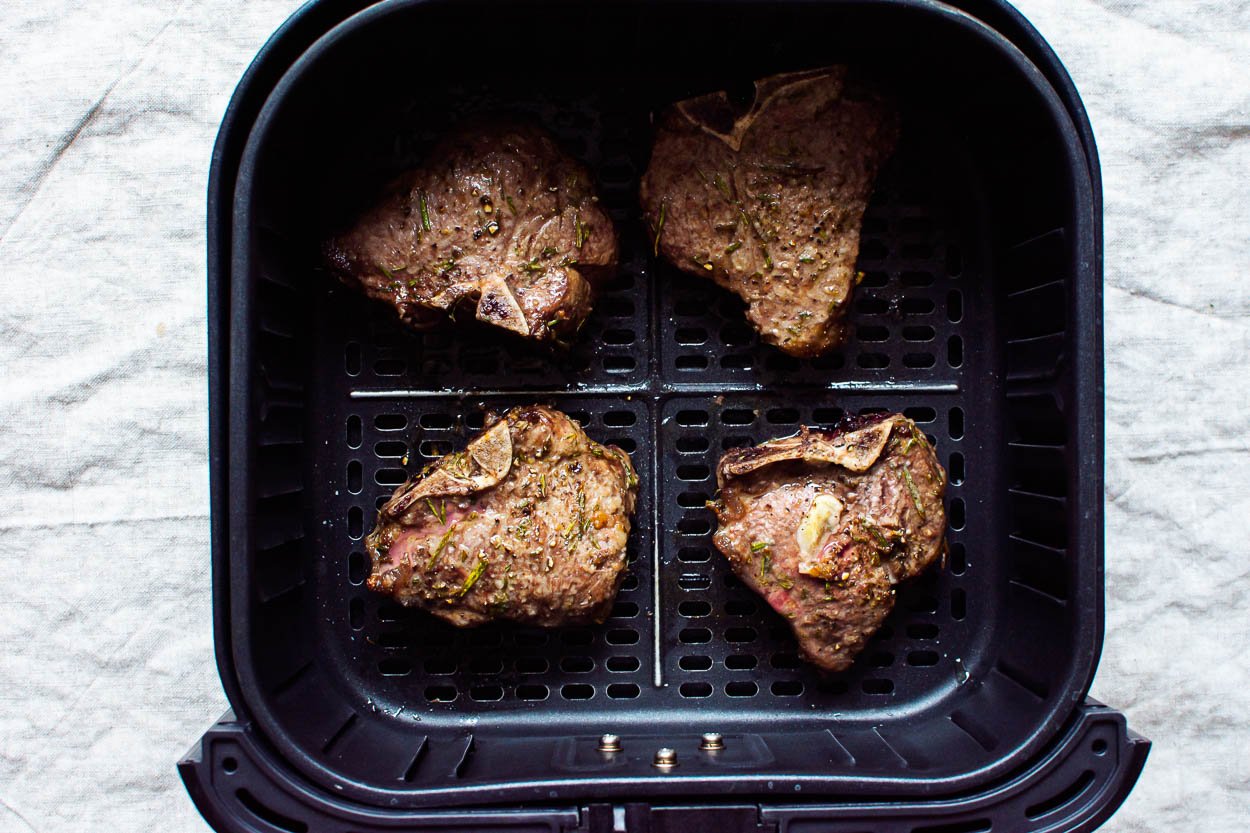 Four cooked lamb chops in the air fryer basket.