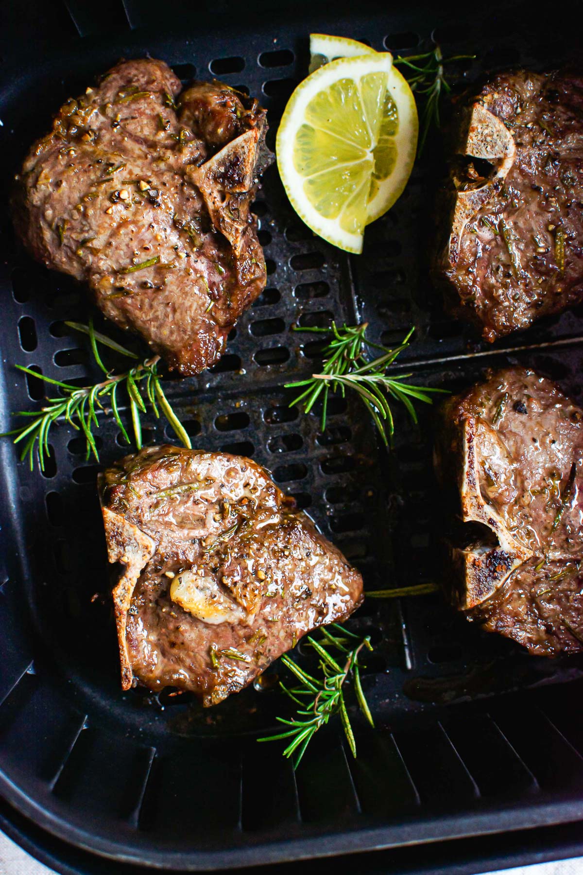 Lamb chops in air fryer with rosemary sprigs and lemon.