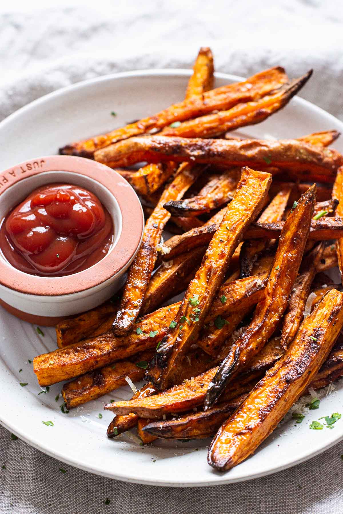 Crispy air fryer sweet potato fries on plate with small bowl of ketchup.