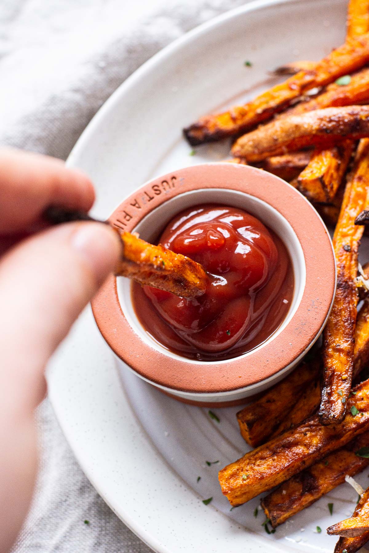 Air fryer sweet potato fries being dipped into ketchup.