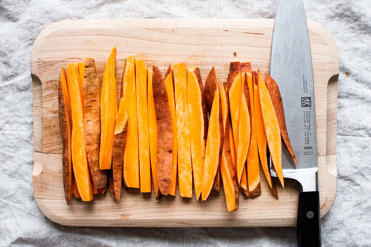 Sweet potato cut into 1/4 inch sticks on cutting board.