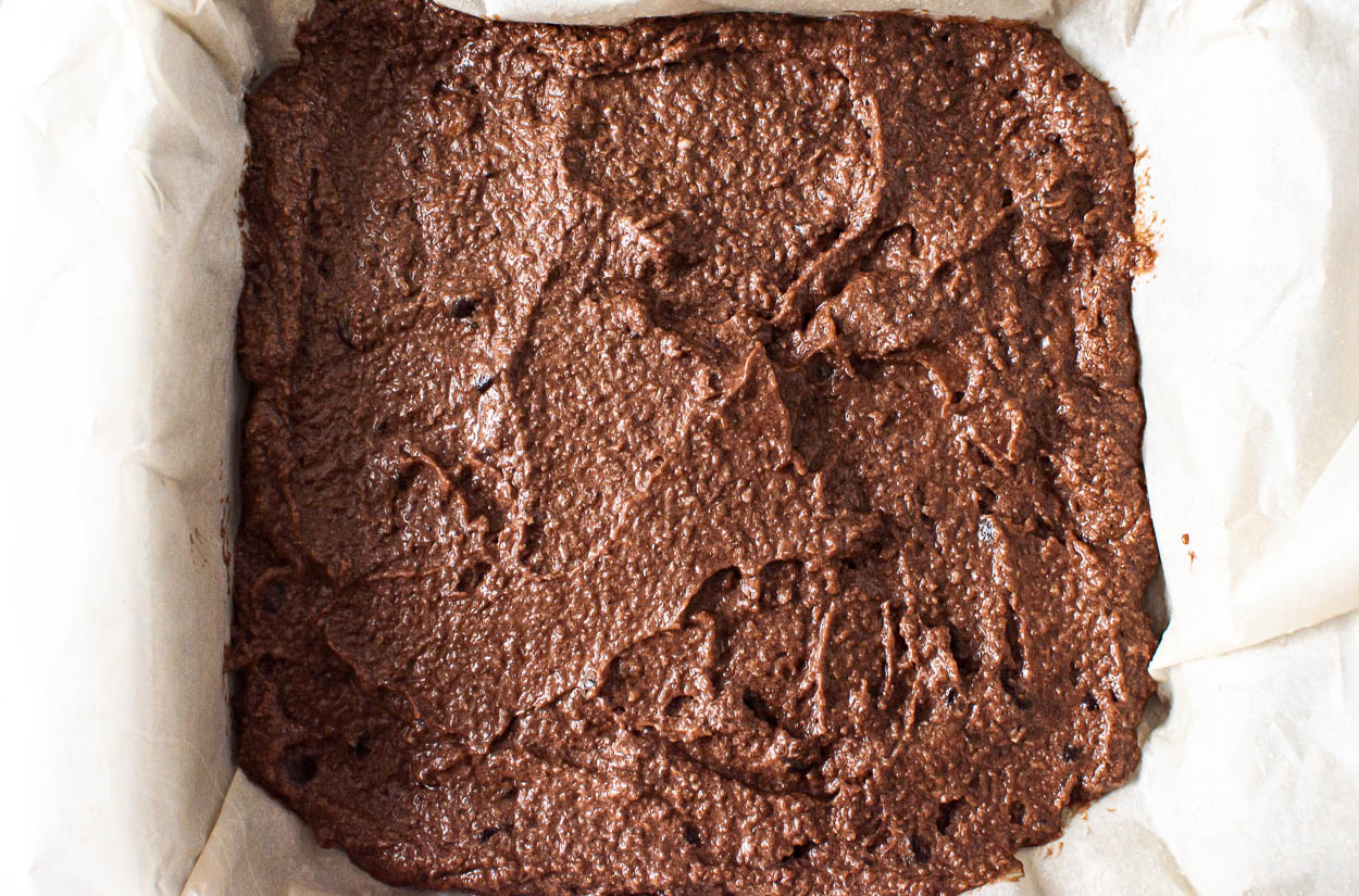 Brownie batter in baking dish lined with parchment paper.