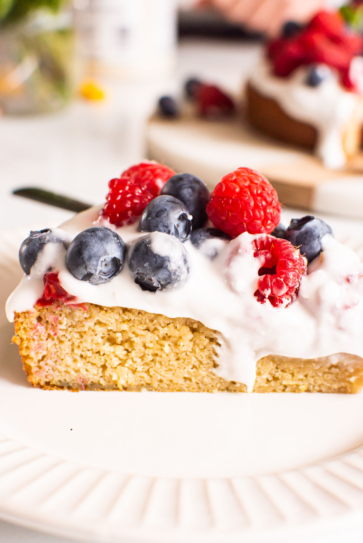 Slice of cake on plate with whipped topping, blueberries and raspberries.
