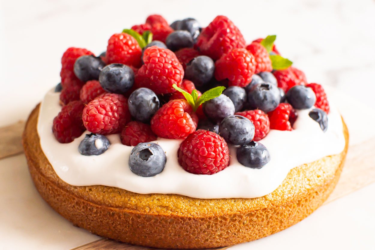 Cake topped with coconut whipped cream, fresh berries, and mint leaves.