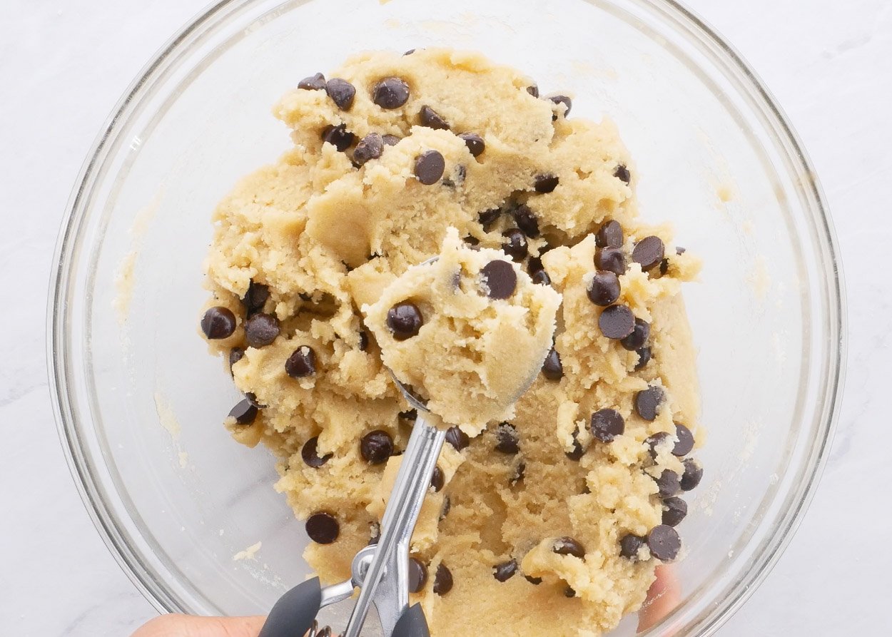 Stirring chocolate chips into cookie dough batter in a bowl.