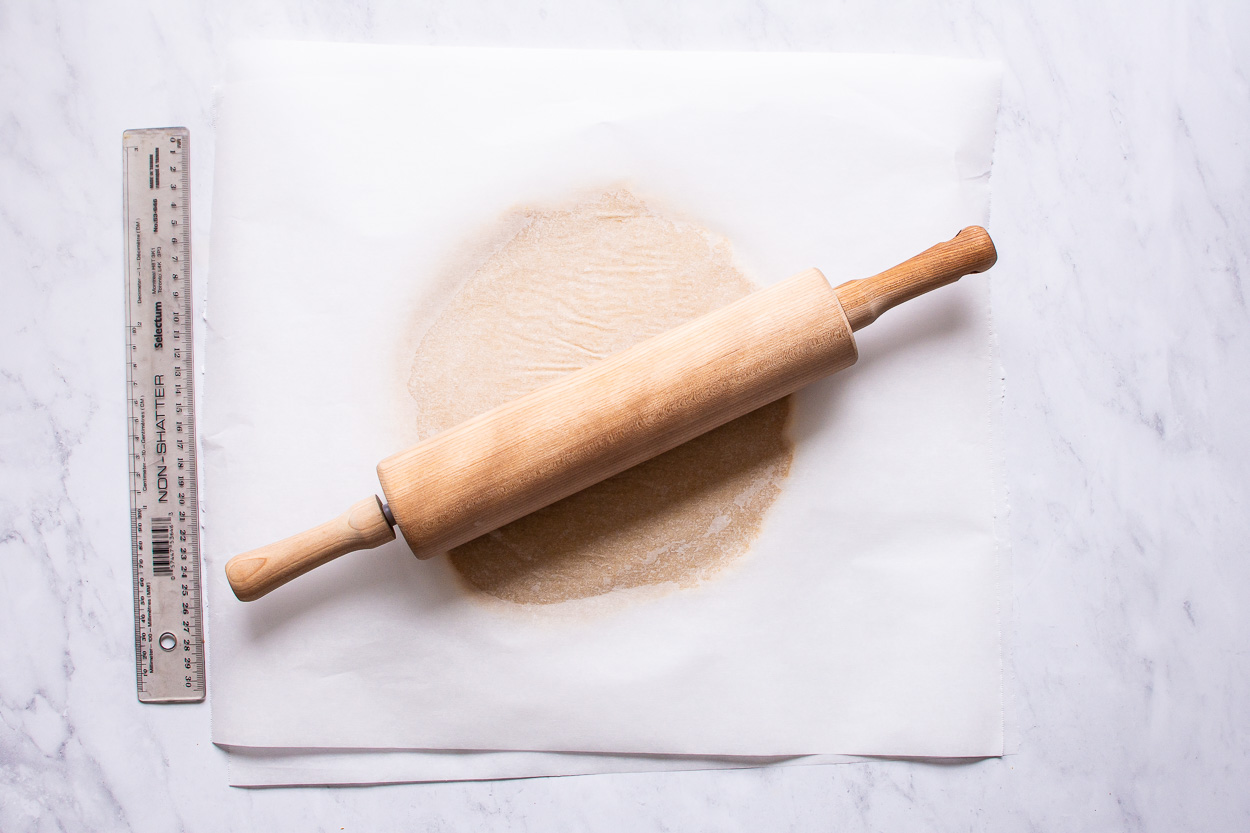Rolled almond flour pizza crust between two pieces or parchment paper.