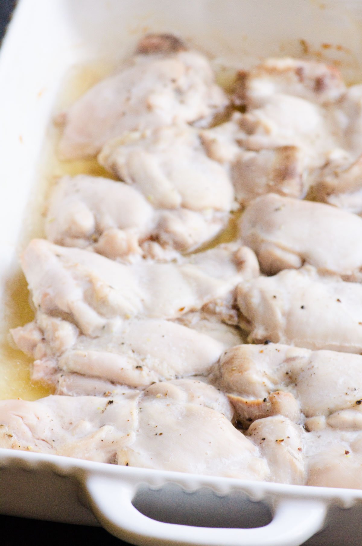 Baked chicken thighs with juices in baking dish.