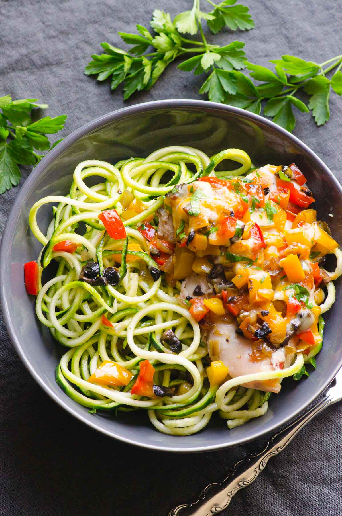 Chicken and peppers with zoodles in bowl with parsley in background.