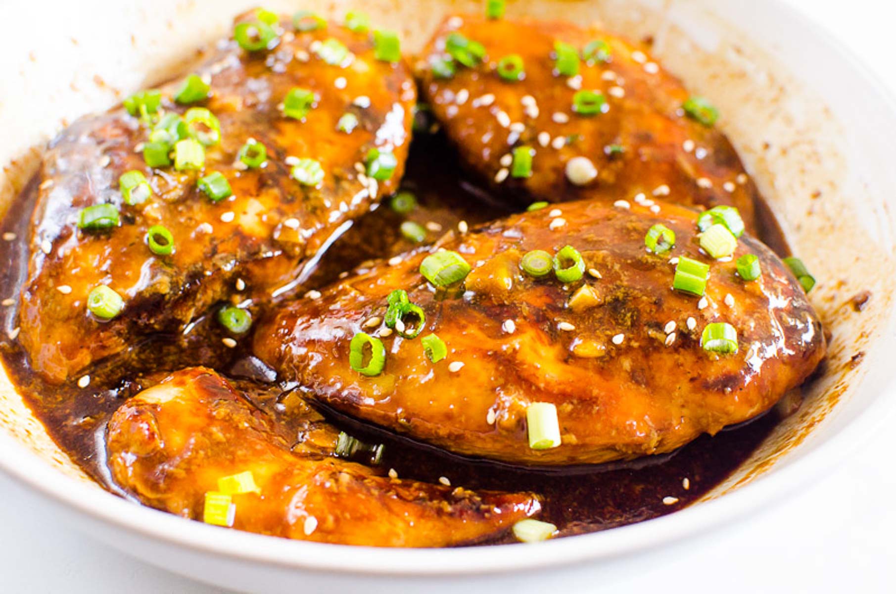 Chicken with sauce and green onion and sesame seed garnish in baking dish.