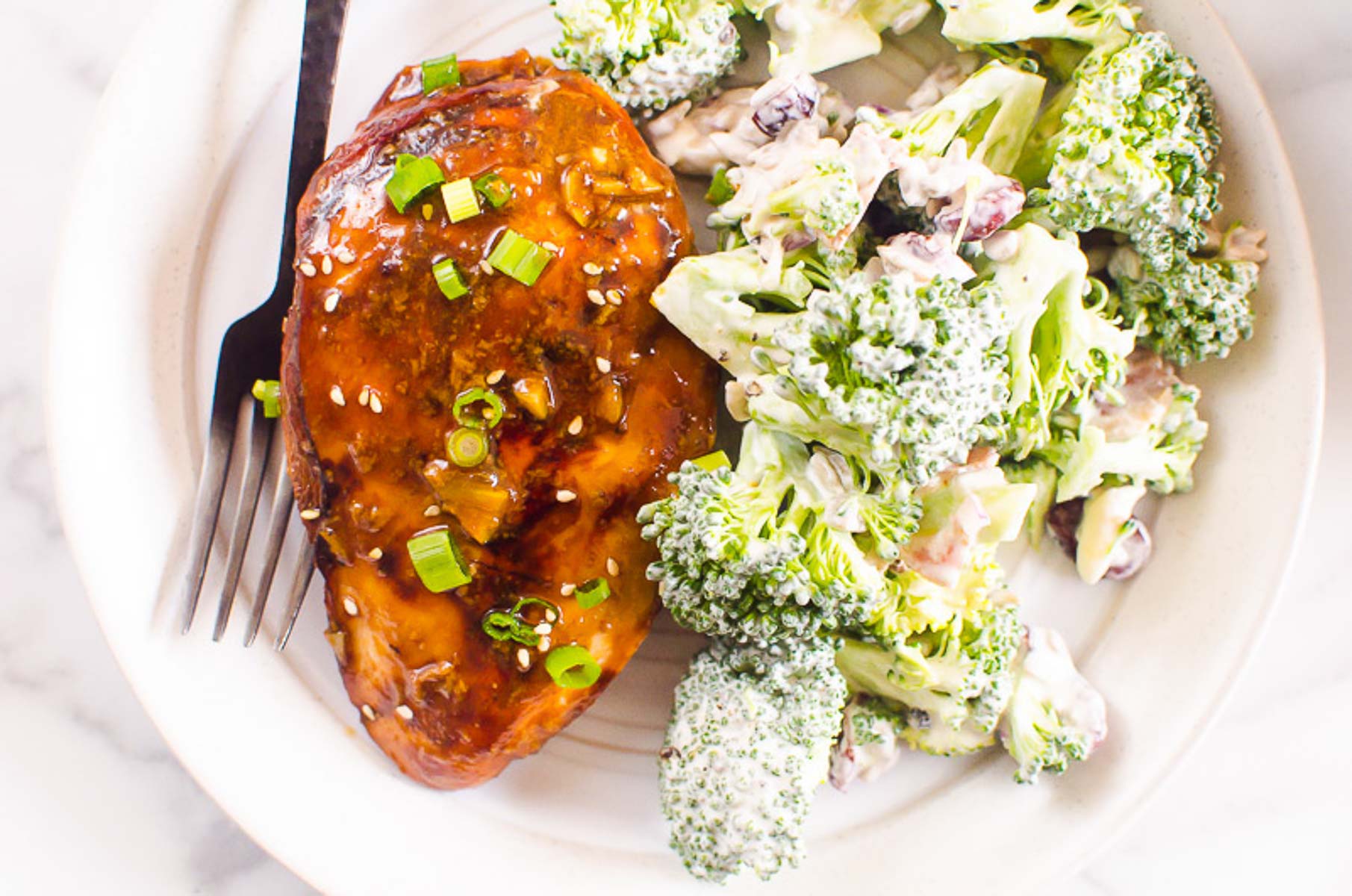 Baked honey garlic chicken breast on a plate with broccoli salad.