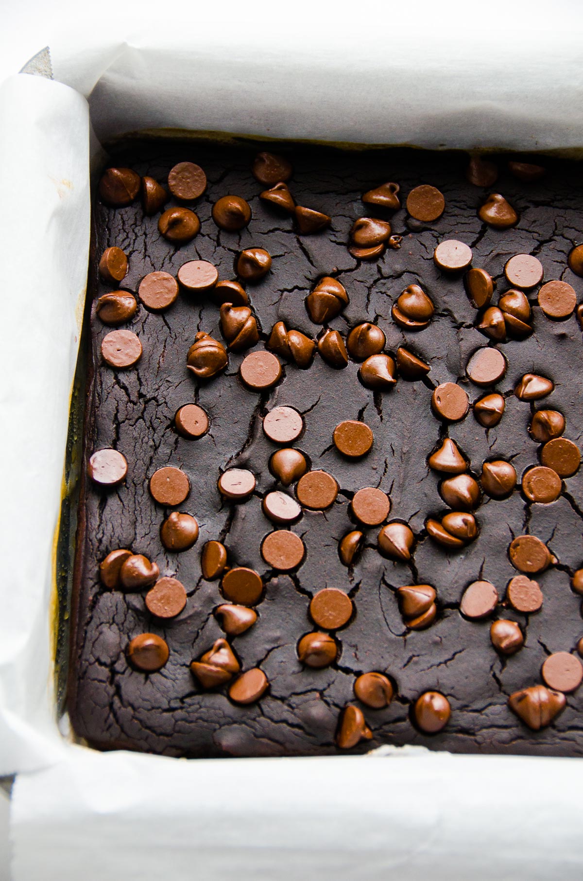 Parchment lined pan of black bean brownies with chocolate chips. 