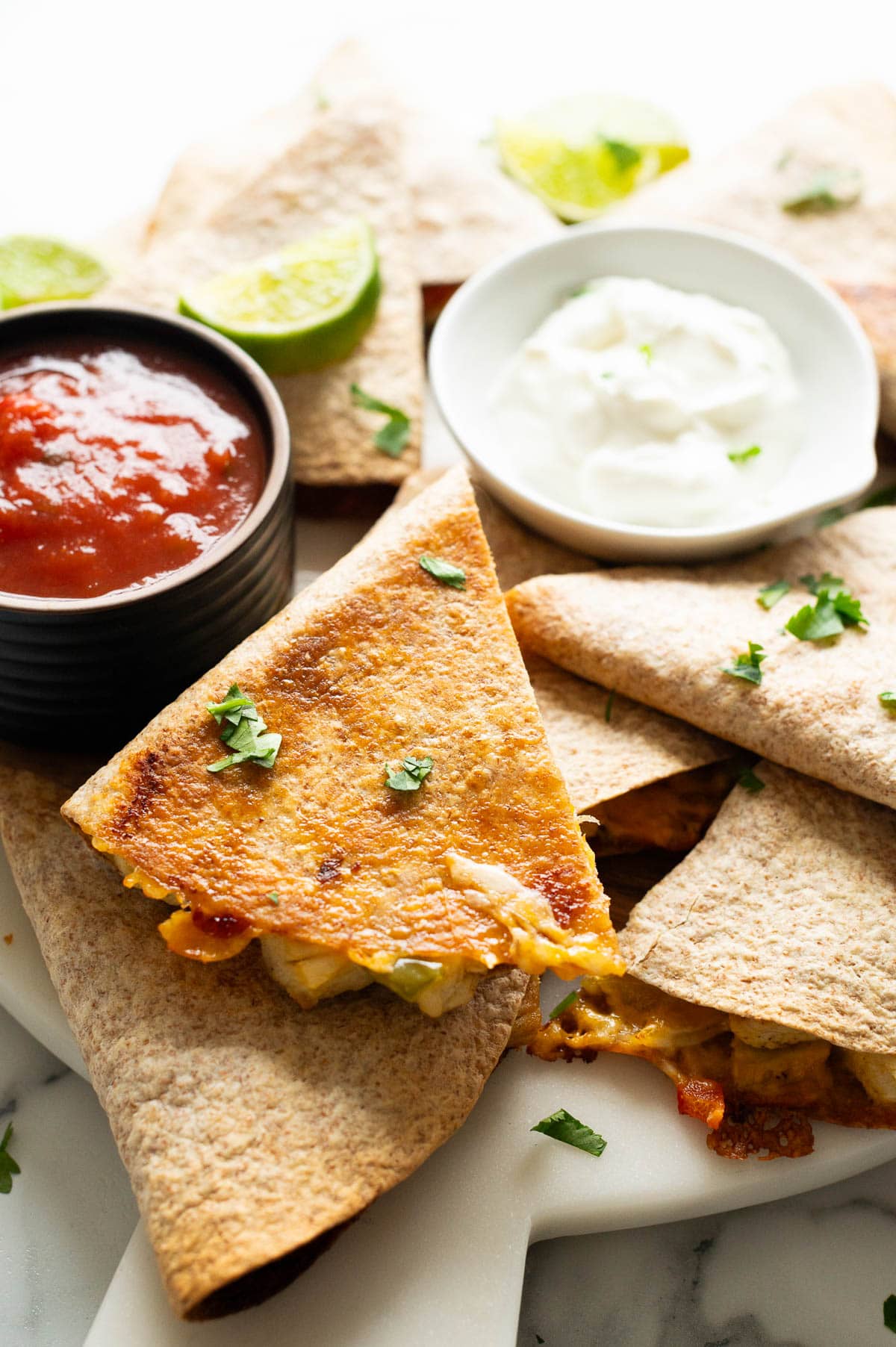 Cut up chicken quesadillas served with salsa and sour cream.