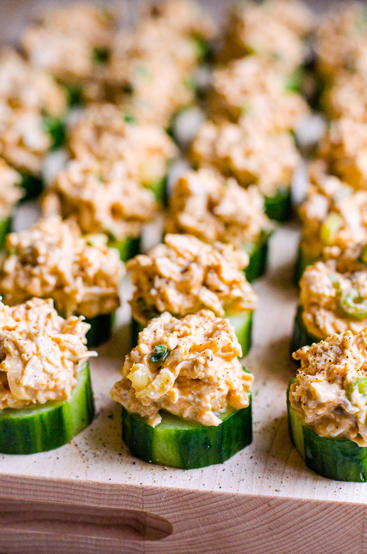 Cucumber snacks with buffalo chicken in a row on wood cutting board.