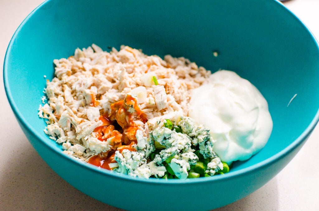 Chicken, yogurt, blue cheese, onion and pepper in blue bowl.