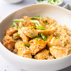 orange chicken in a bowl with quinoa and sesame seed green onion garnish