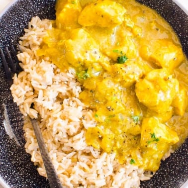 Yellow chicken curry garnished with cilantro and served with rice in a bowl.