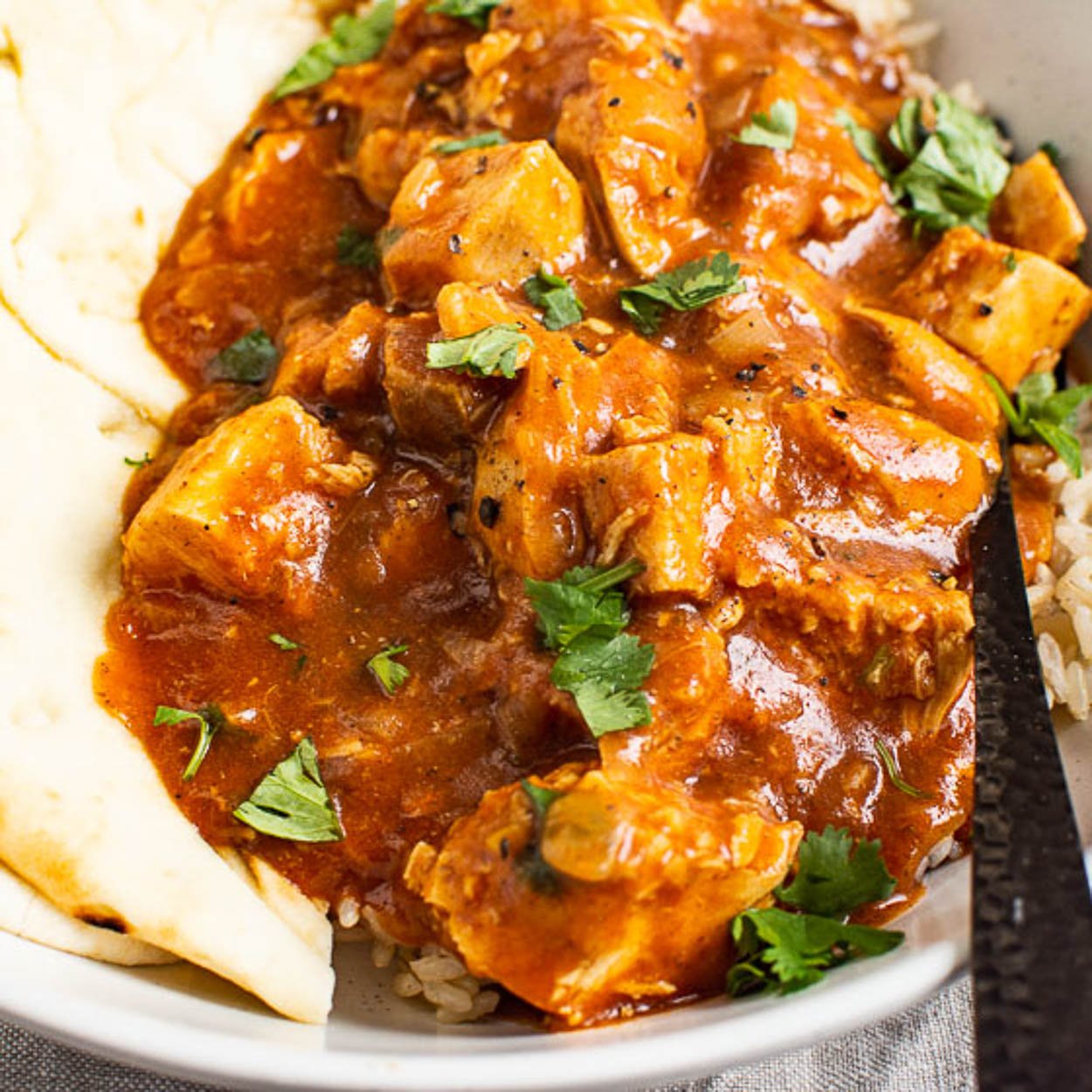 Instant Pot butter chicken in a bowl with naan, rice and cilantro garnish.