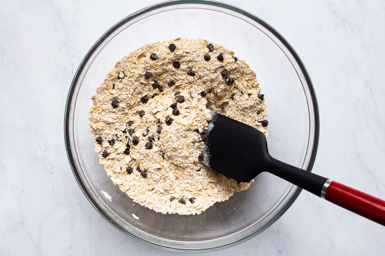 Oat flour, oats, and chocolate chips in bowl with spatula.