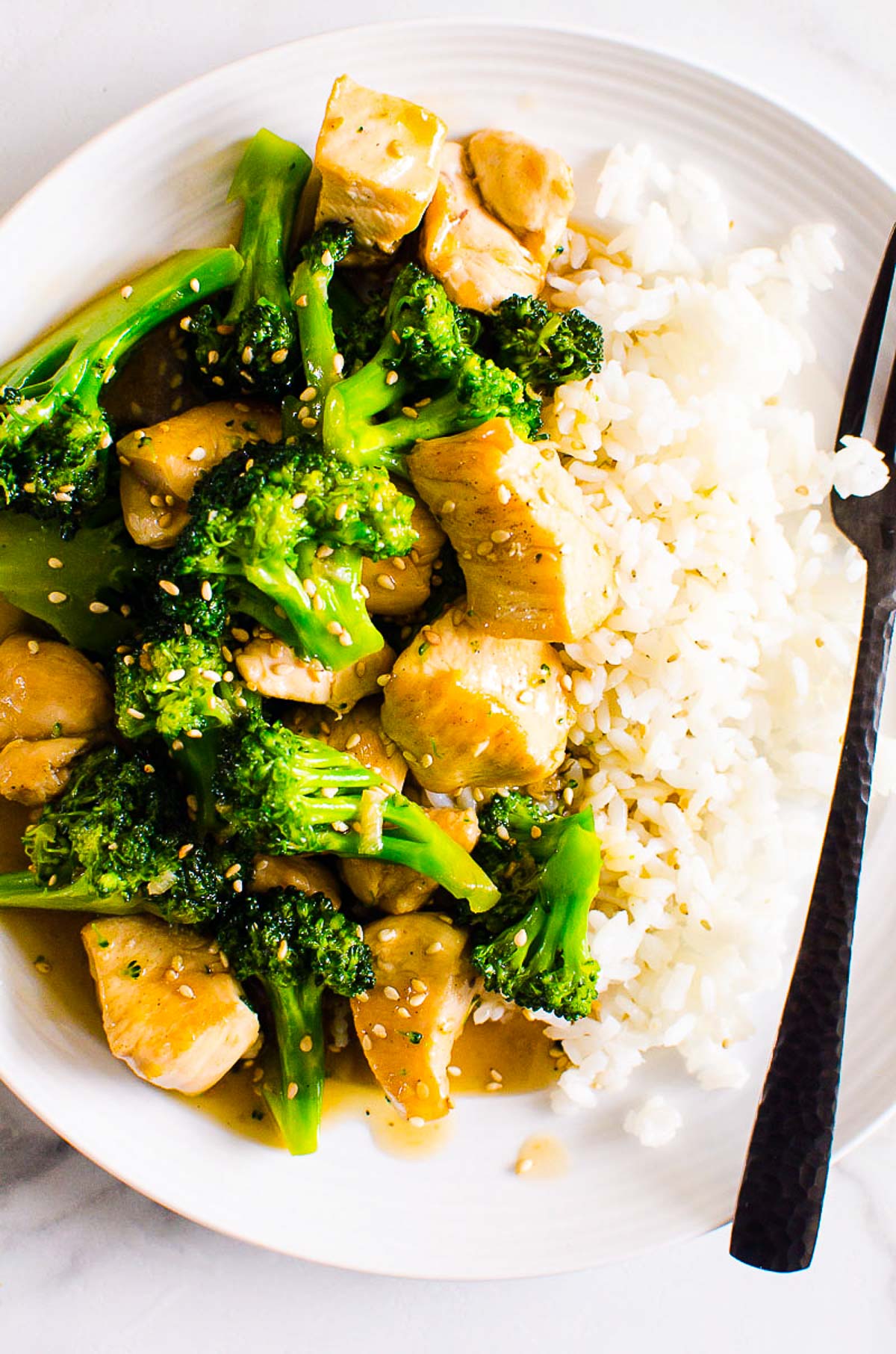 Chicken broccoli stir fry served with rice and sesame seeds and black fork.