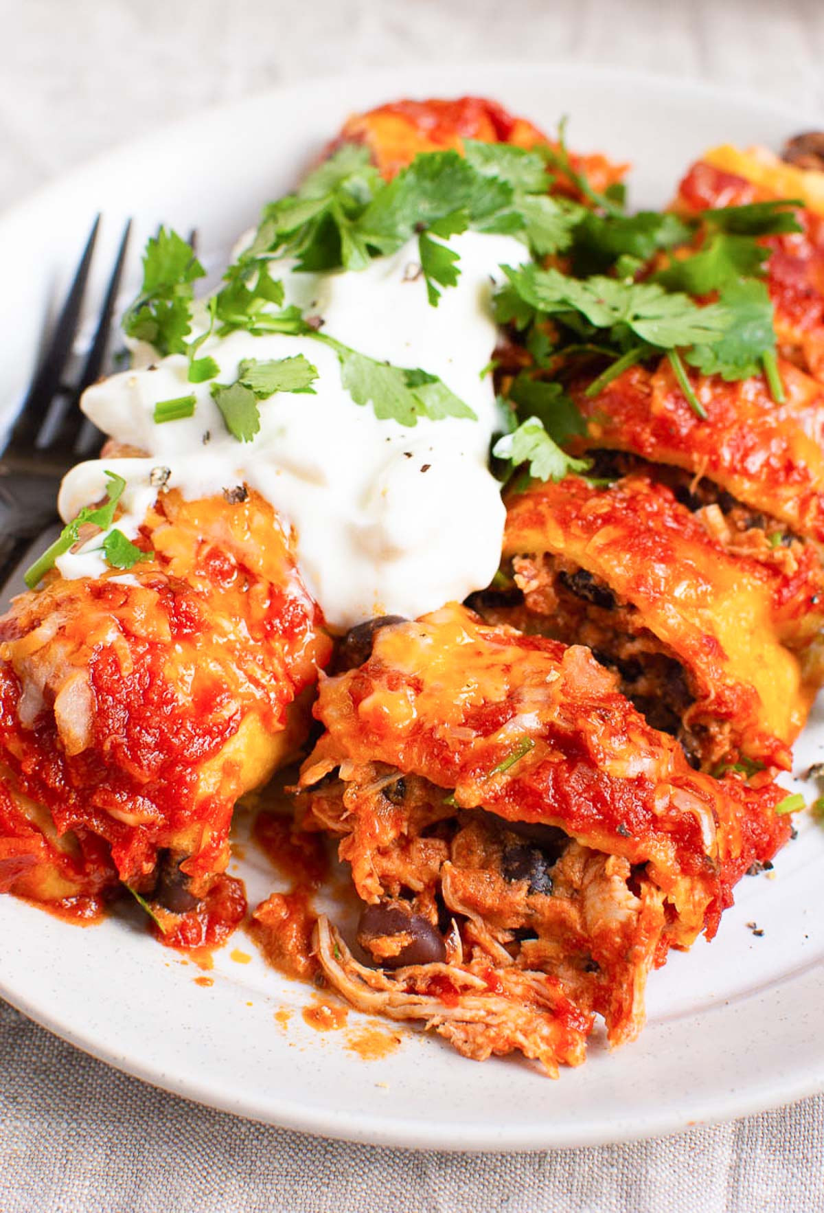 Two healthy chicken enchiladas on a plate with sauce, cheese and sour cream.