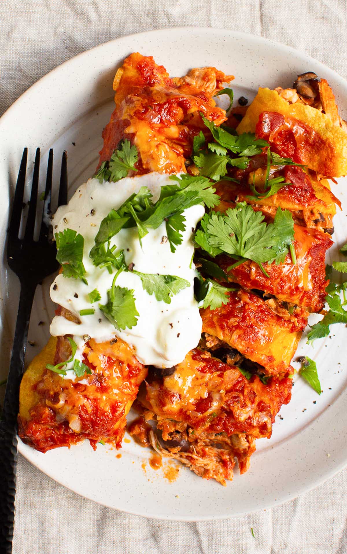 Healthy chicken enchiladas on a plate with sour cream and cilantro.