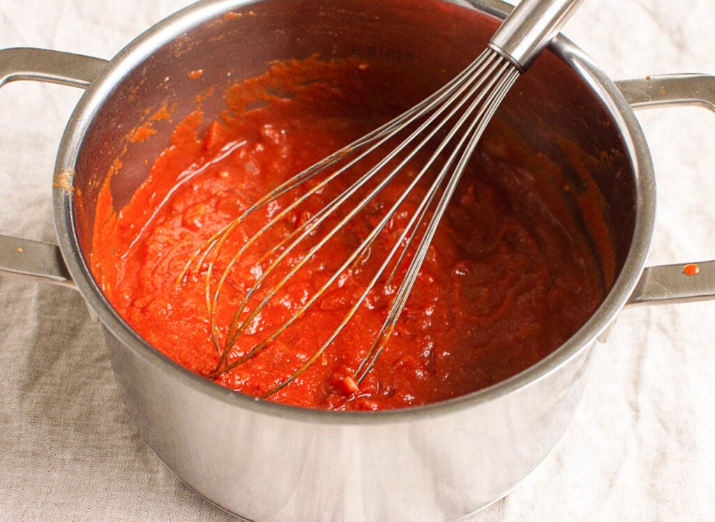 Stirring tomato sauce and seasoning in stovepot.