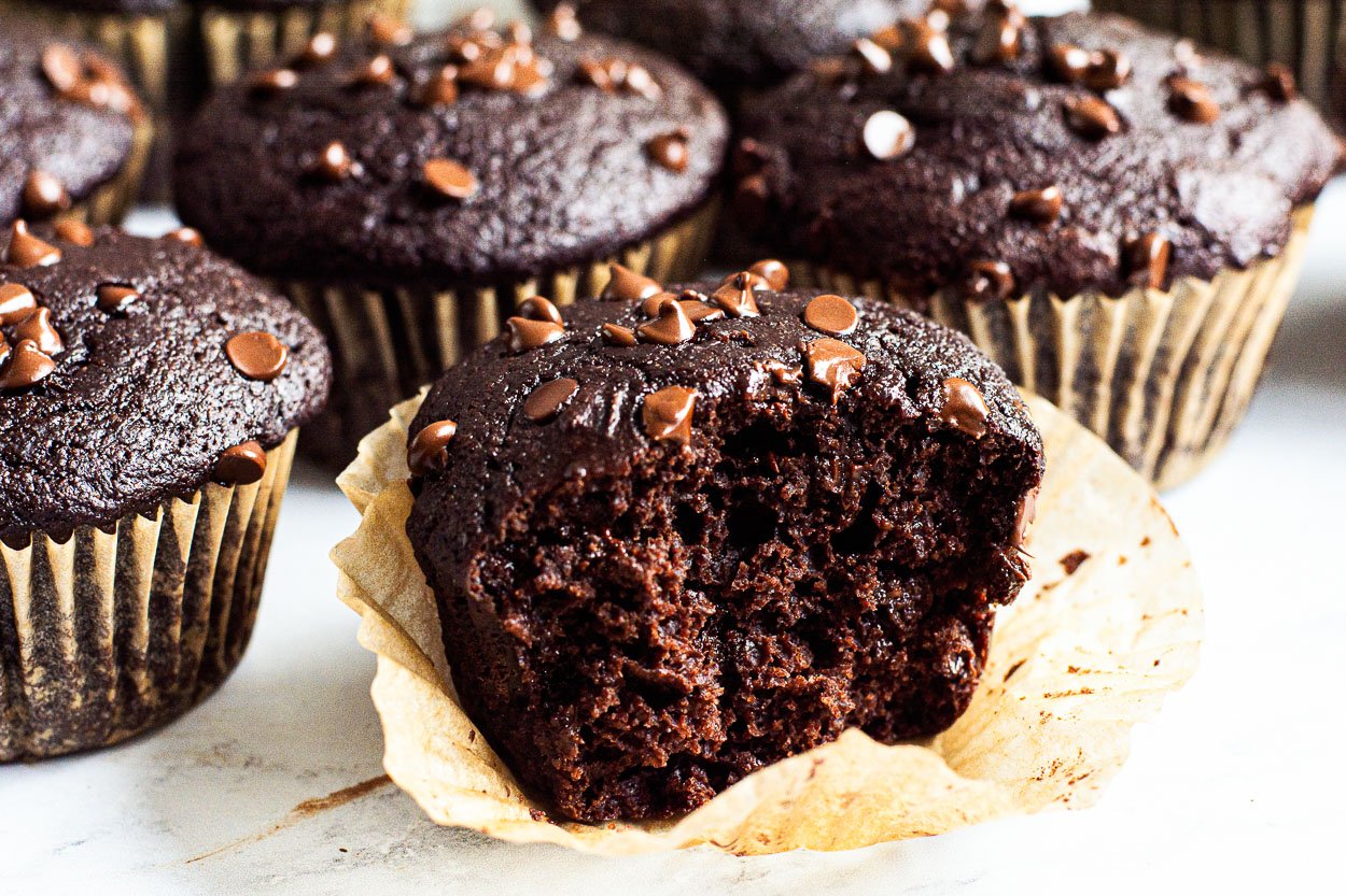 Chocolate muffins with one unwrapped with a bite missing.