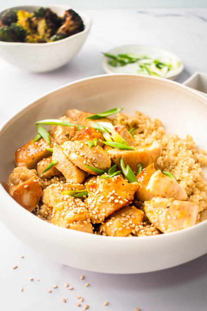 healthy orange chicken garnished with sesame seeds and green onion in a bowl for serving with quinoa