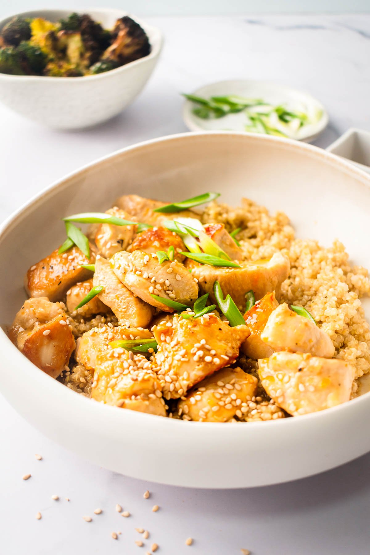 Healthy orange chicken garnished with sesame seeds, green onion in bowl with quinoa.
