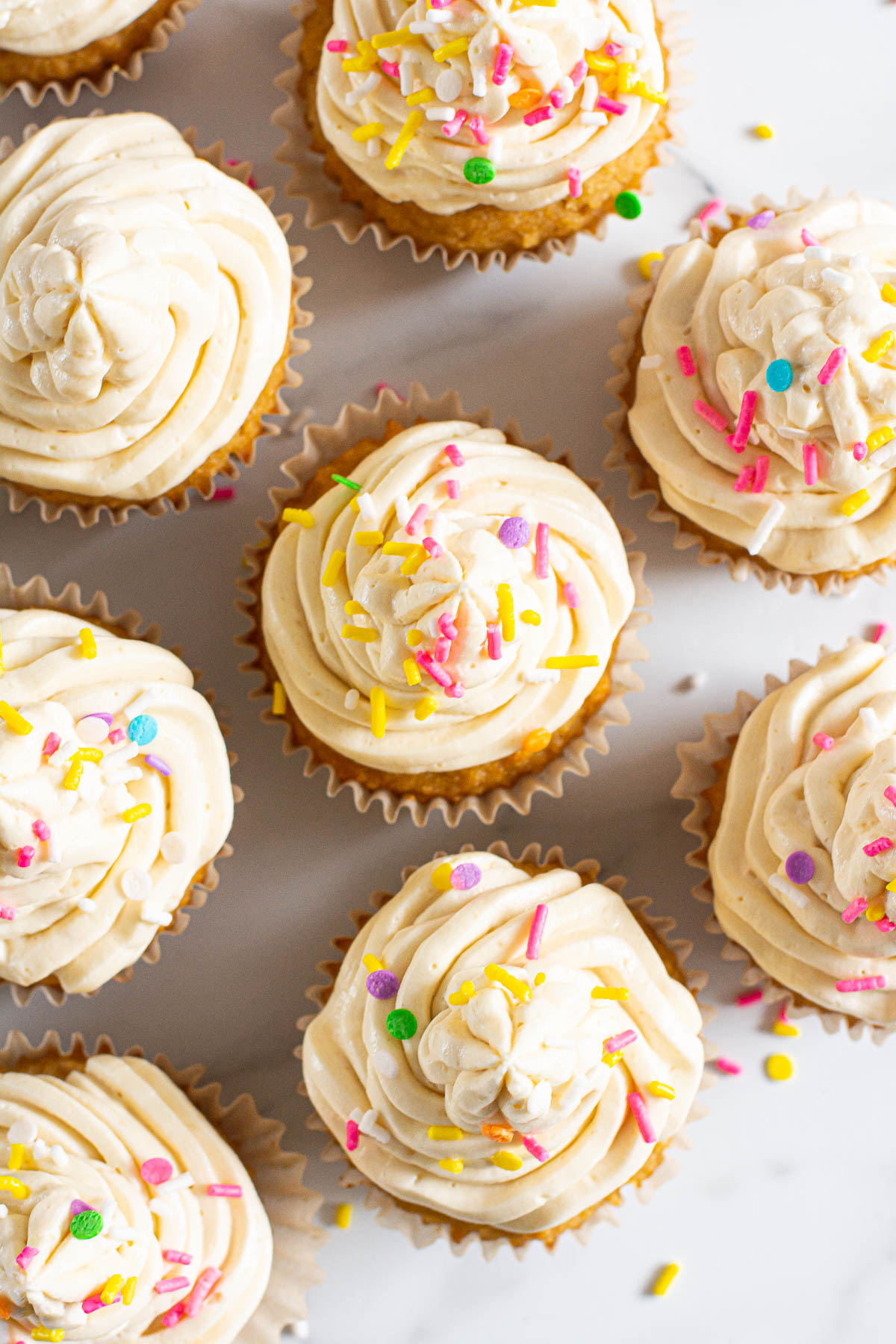 Looking down at healthy vanilla cupcakes with frosting and sprinkles.