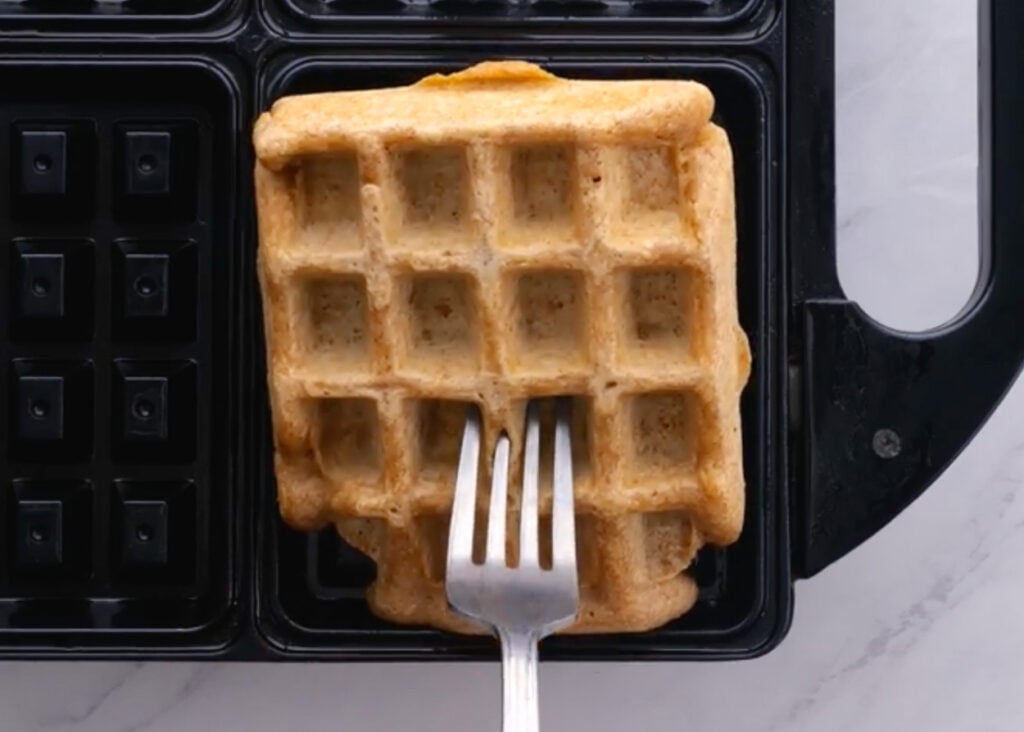 Removing healthy waffles from the griddle with a fork.