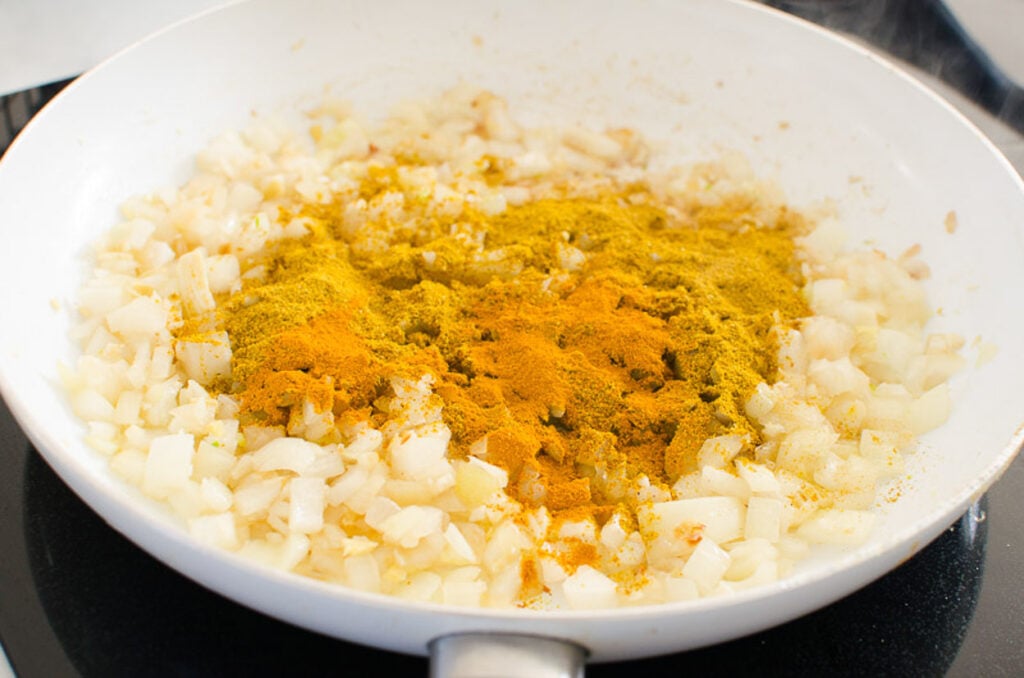 Turmeric and curry powder added to onion in skillet.