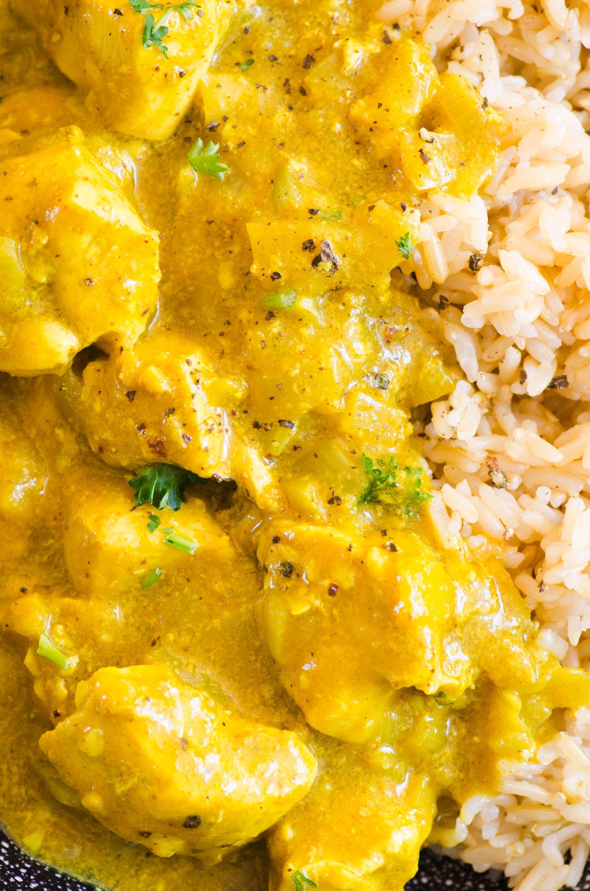 Yellow chicken curry with rice and cilantro and black pepper garnish.