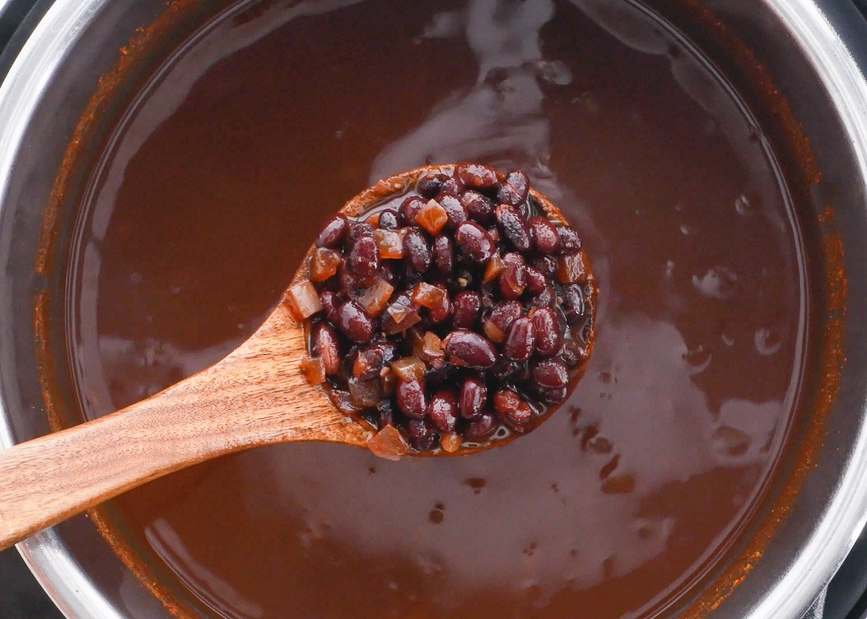 Cooked black beans on wooden spoon above the pot.
