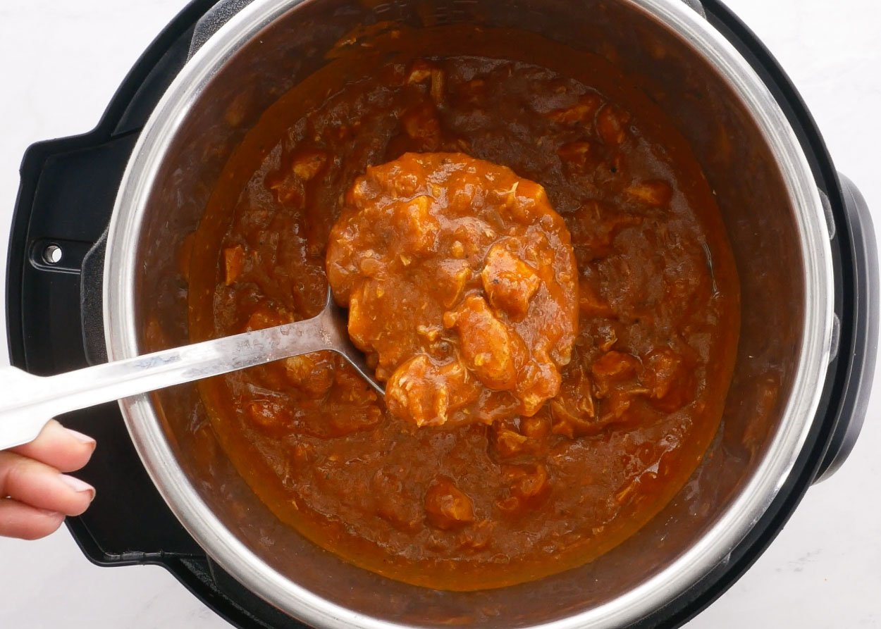 Scooping butter chicken with a ladle from pressure cooker.
