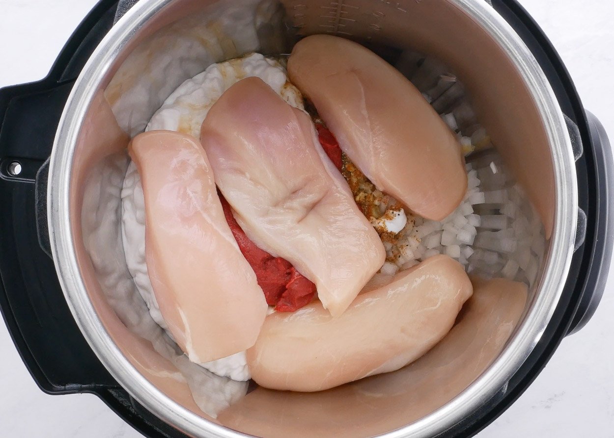 Spices, onion, coconut milk, tomato paste and raw chicken breasts inside Instant Pot.