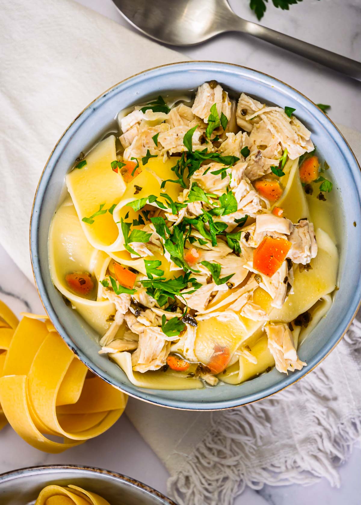 Instant pot chicken noodle soup with parsley in blue bowl.