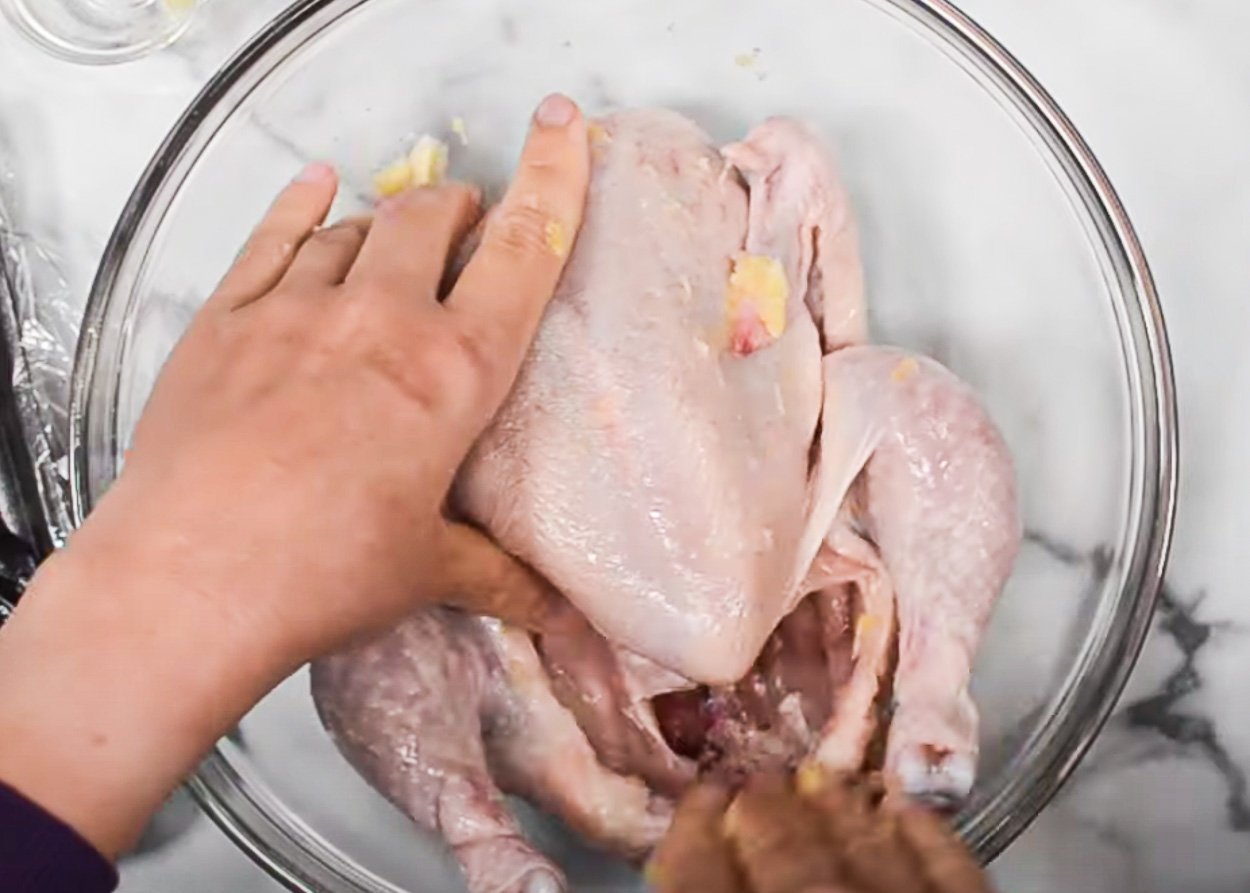 Rubbing whole chicken with freshly grated garlic in glass bowl.