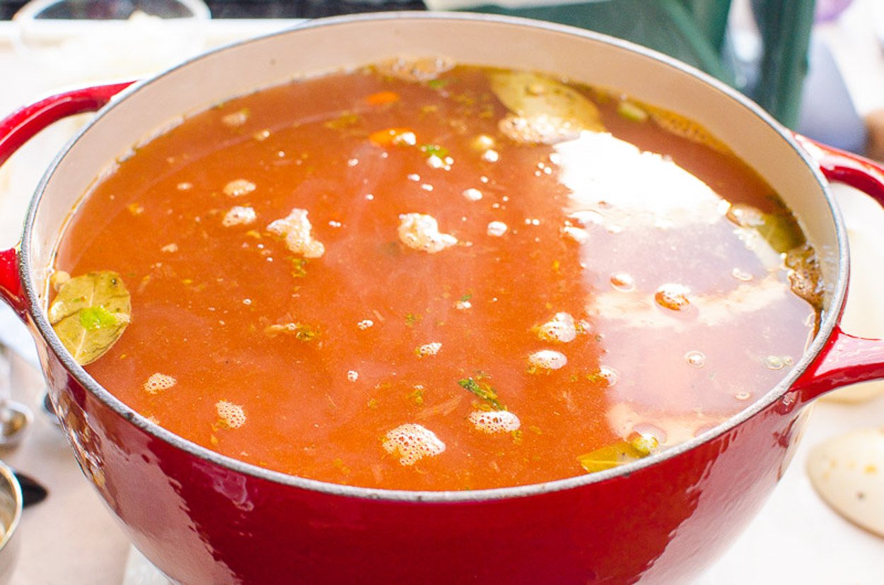Red pot filled with lentil soup ingredients including broth.