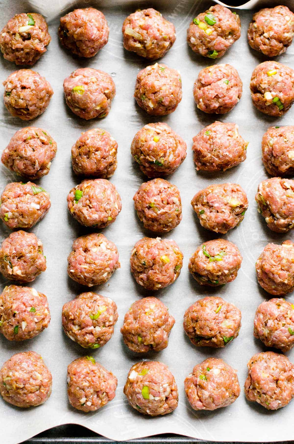 Raw meatballs on parchment lined baking pan. 
