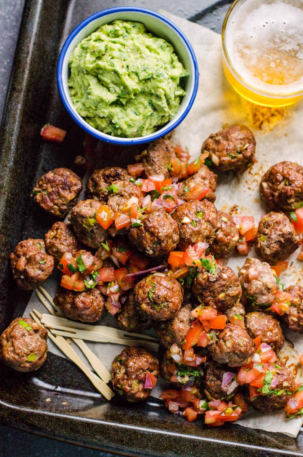 Mexican meatballs on a serving tray with guacamole and beer.