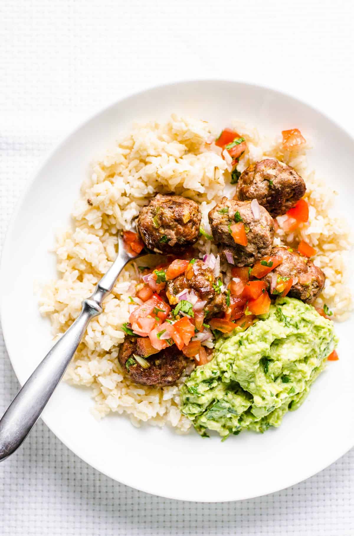 Mexican meatballs garnished with pico and served over rice on a plate.