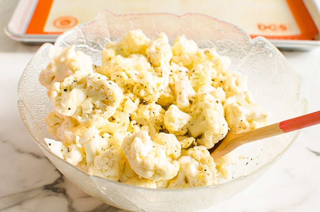 mixing cauliflower in a bowl with seasonings for roasting in oven